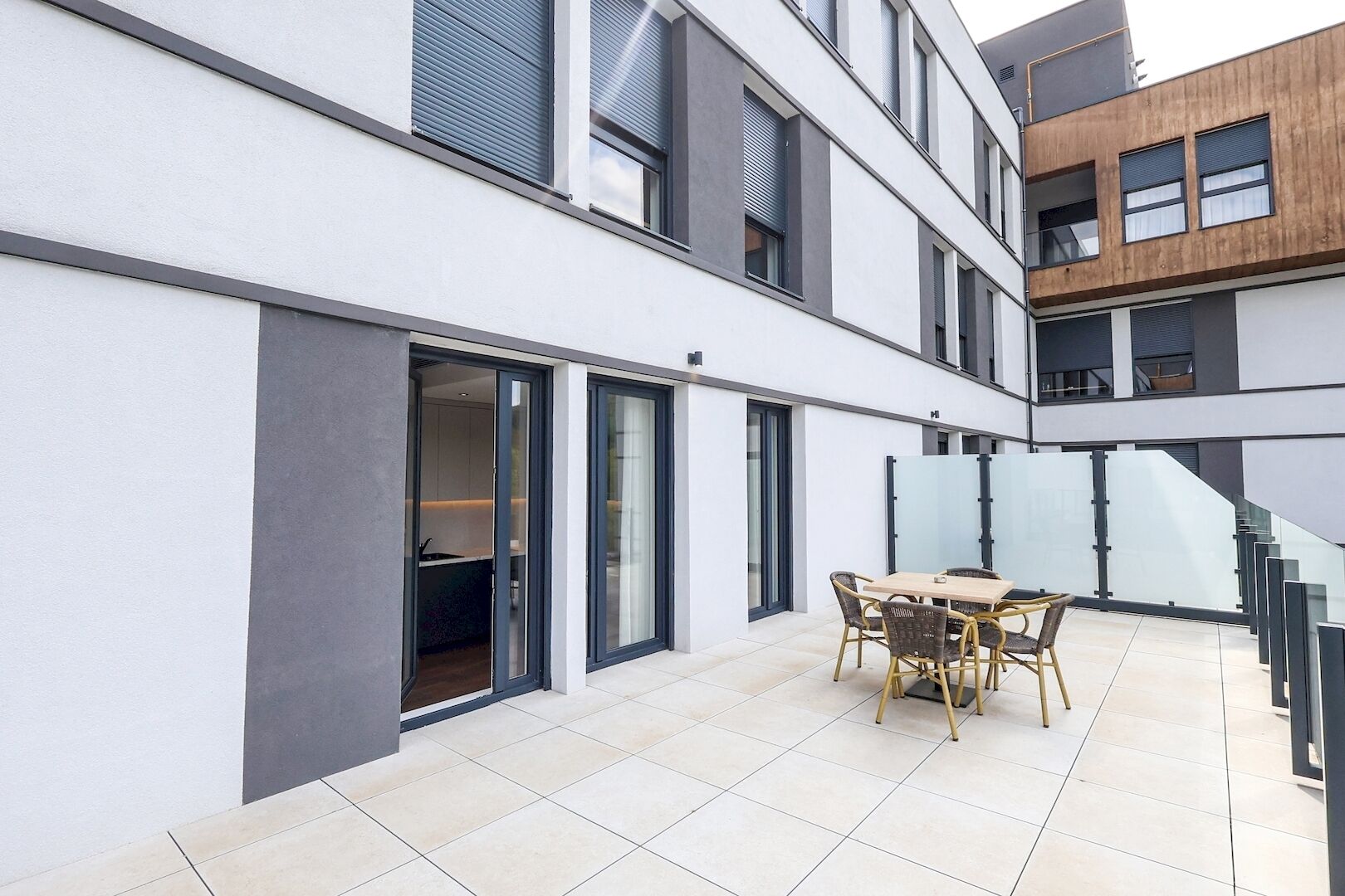Un edificio moderno con un patio que cuenta con una mesa, sillas, barandilla de vidrio y una escalera.