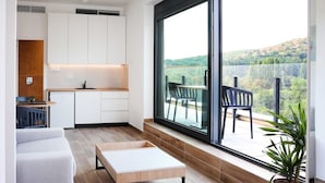Et moderne køkken med hvide skabe, et spiseområde med bænk og et stort vindue med udsigt til et naturskønt landskab.