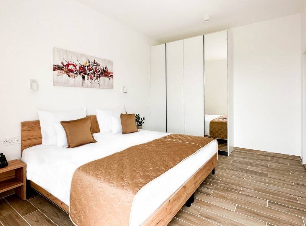 A modern hotel room with a large bed, a wooden headboard, a bedside table, and a wardrobe.