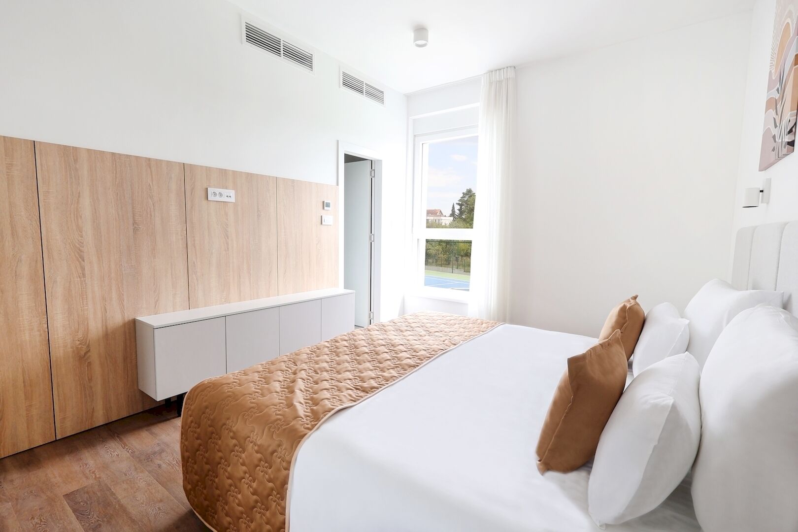 Une chambre d’hôtel moderne avec un grand lit, une armoire en bois et une vue sur un court de tennis.