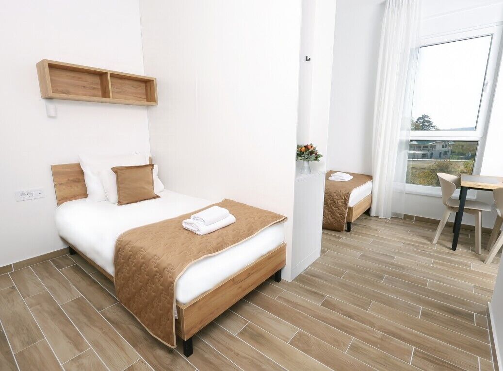 A modern hotel room with a wooden bed, a small desk, and a window with a view.
