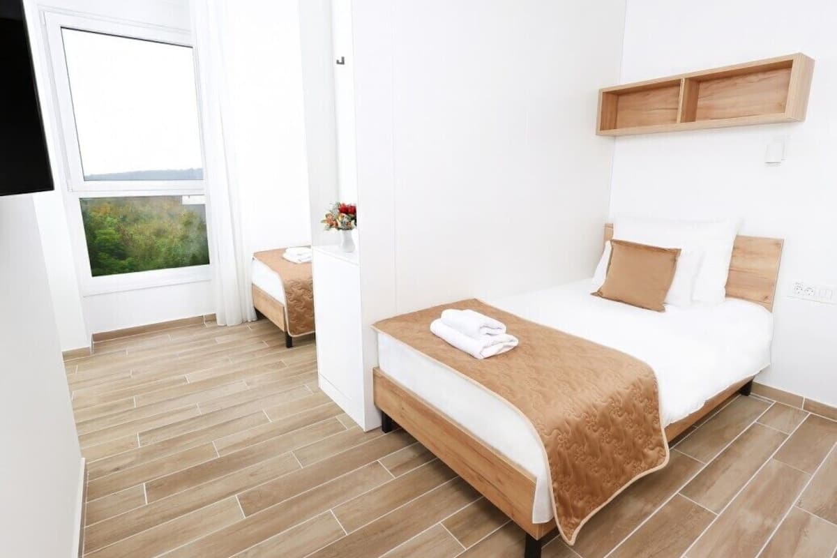 Un dormitorio con una cama grande, otra más pequeña, un estante de madera y una ventana con vistas.