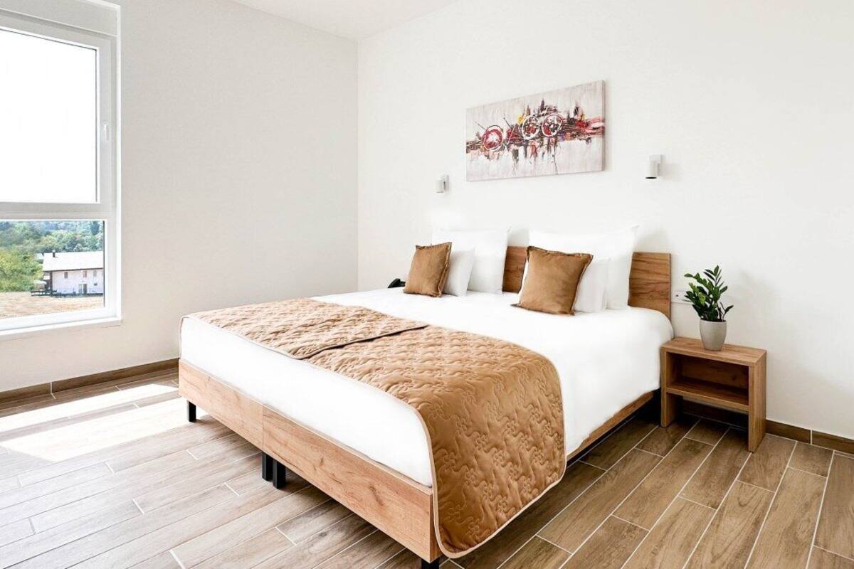 Un dormitorio moderno con una cama grande, una mesita de noche con una planta y un ventanal con vistas al verdor.
