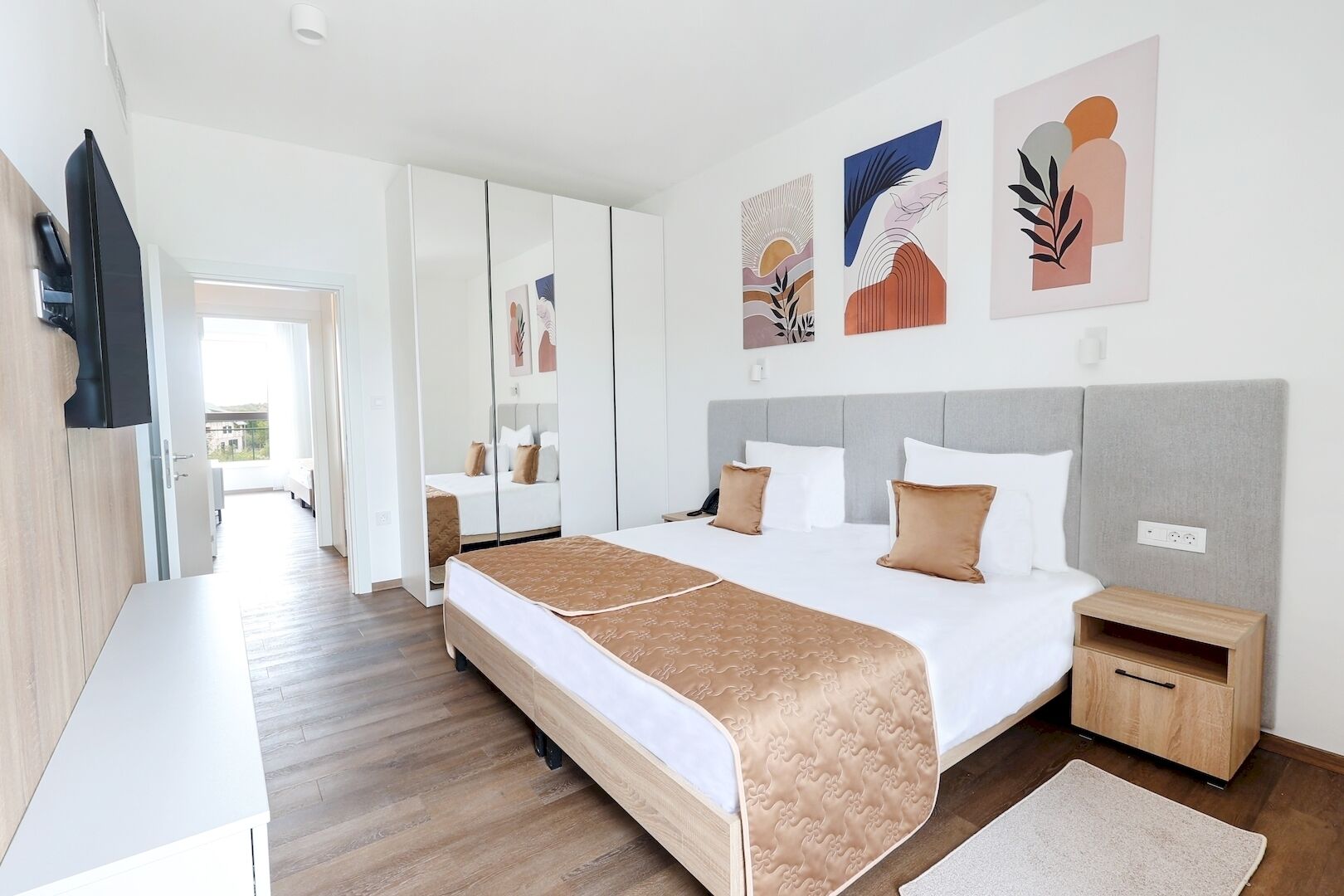 Una habitación de hotel moderna con una cama grande, mesitas de noche, un armario y obras de arte en las paredes.