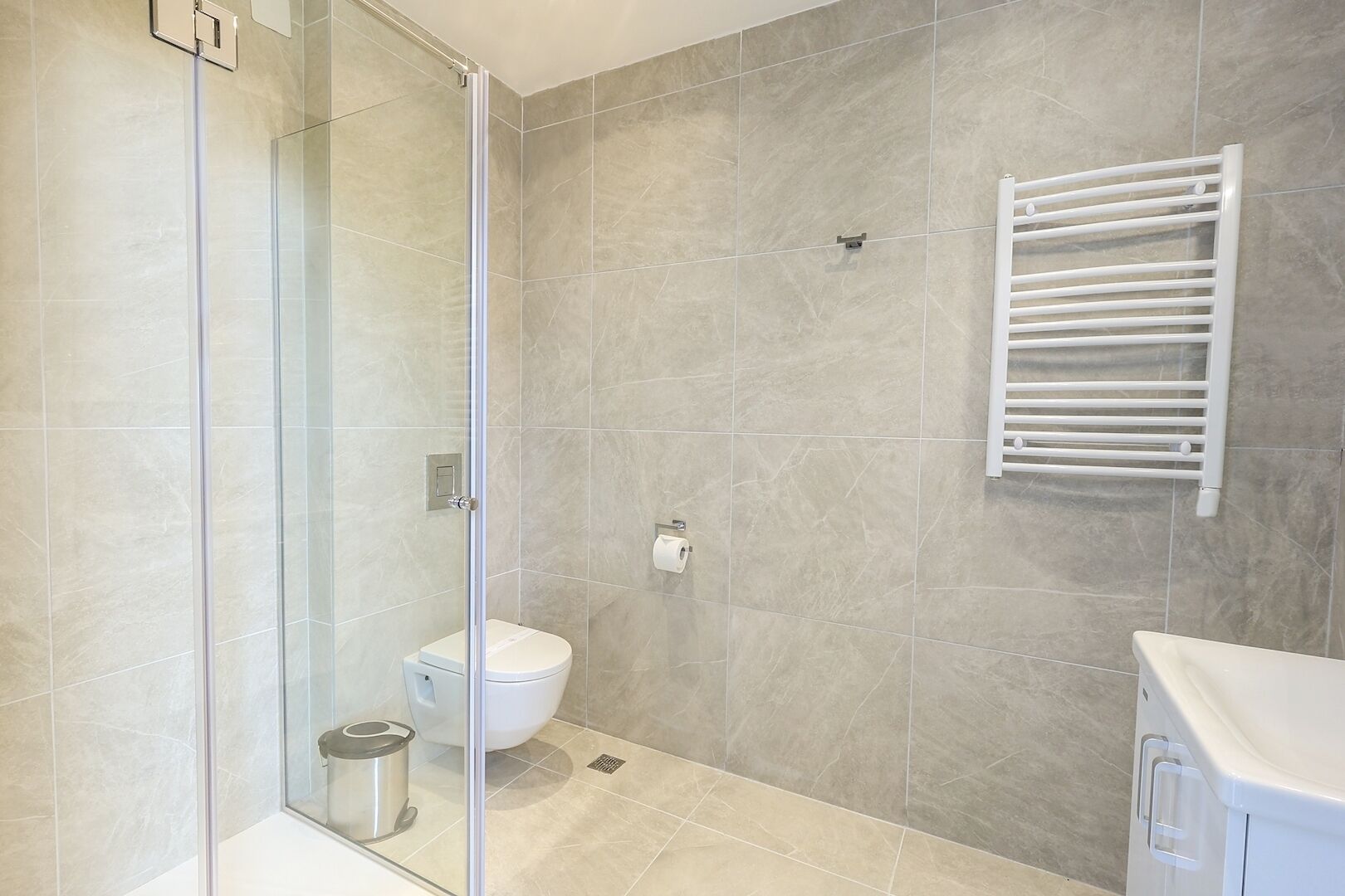 Une salle de bain moderne avec une douche à parois de verre, des toilettes et un porte-serviettes.