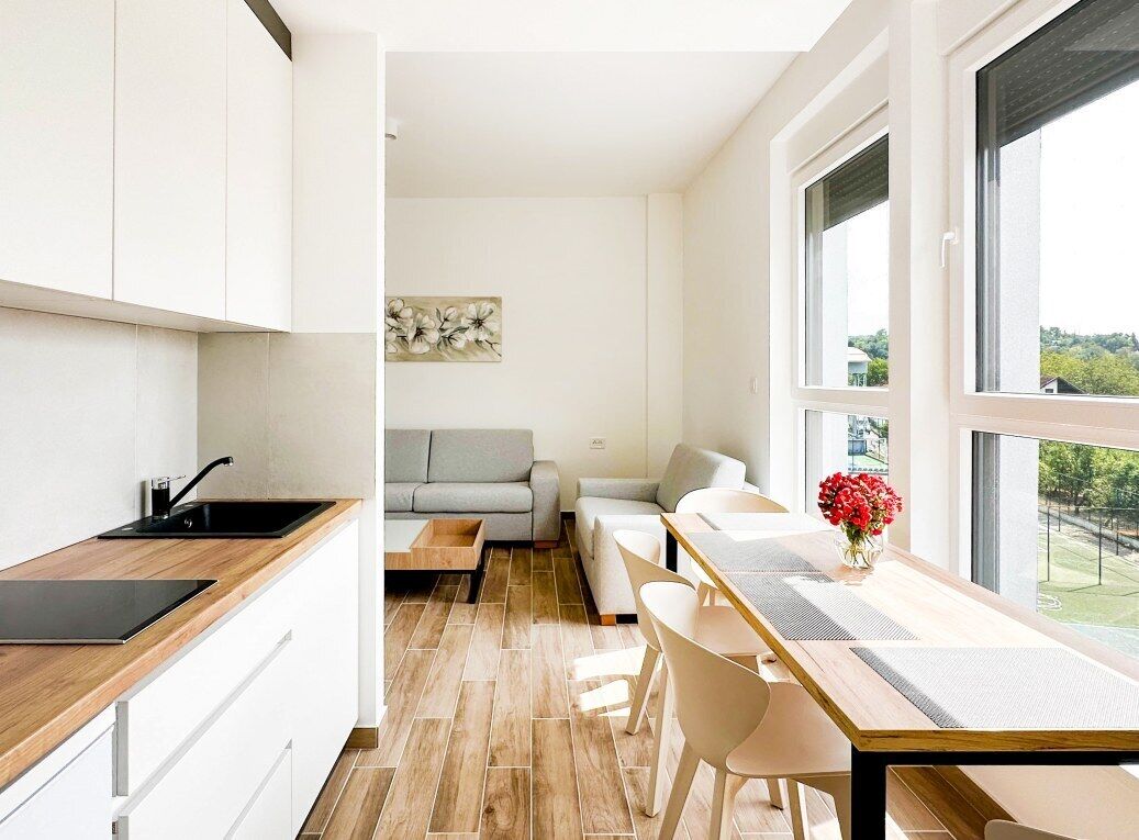 A modern kitchen with a wooden countertop and a black sink. There is a dining area with a table and chairs, and a sofa in the background.