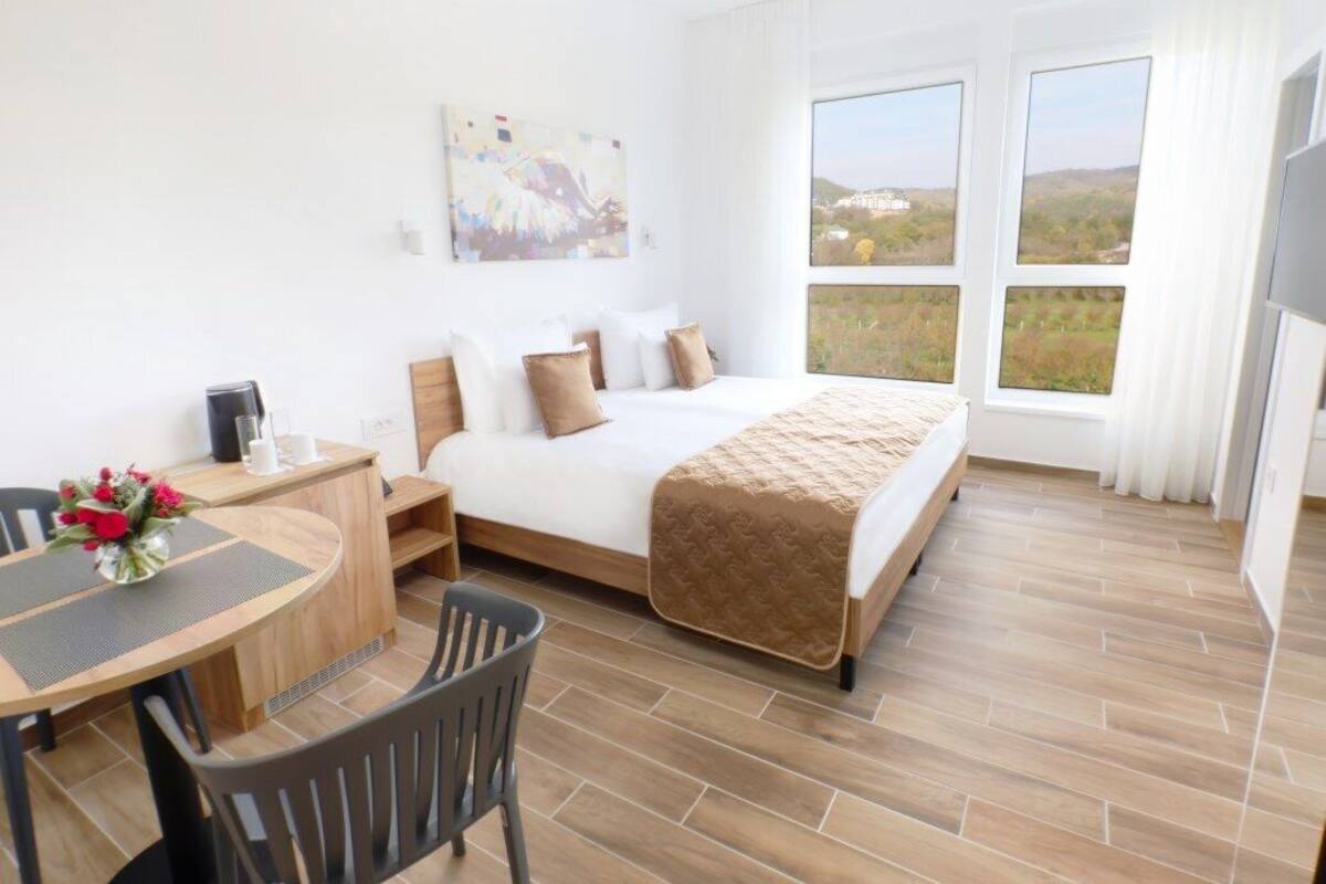 Habitación de hotel con cama, escritorio, silla, ventana con vistas y un cuadro en la pared.