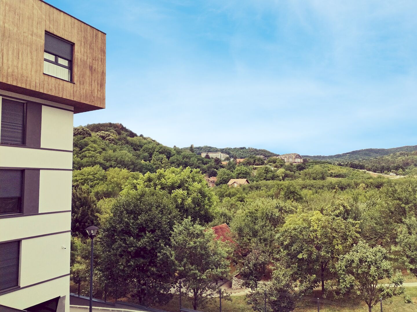 A modern building with a flat roof and large windows, surrounded by lush green hills and trees.