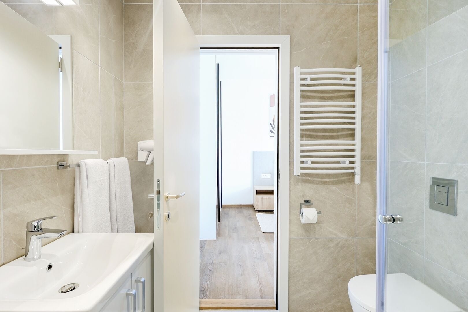 A modern bathroom with a sink, mirror, towel rack, toilet, and shower.