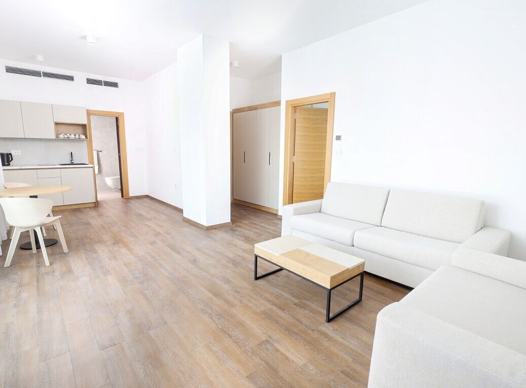 A modern living room with a white sofa, a wooden coffee table, and a dining area with a white chair and table.