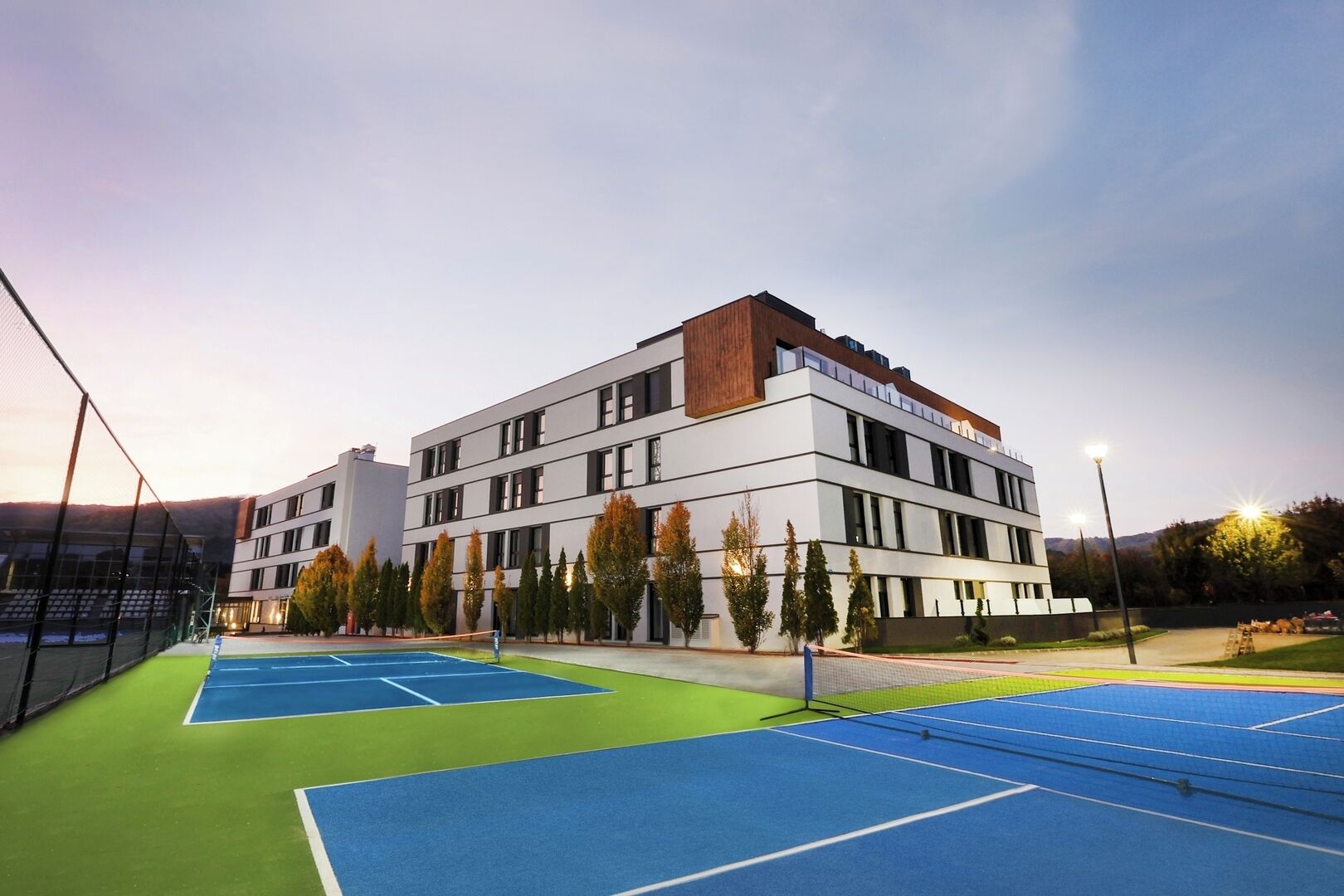 A modern building with multiple tennis courts in front.