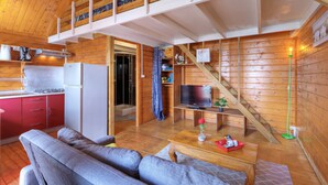 Una cabaña acogedora con habitación en entrepiso, una cocina con armarios rojos, una sala de estar con sofá y mesa de centro, y un televisor.