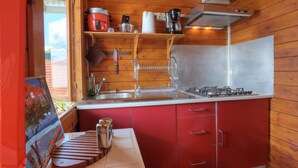 Una cocina compacta con armarios rojos, un lavamanos de acero inoxidable y una estufa a gas.