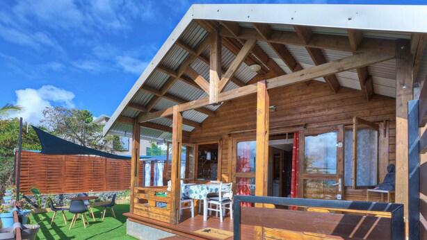Una cabaña de madera con un porche cubierto, mobiliario exterior y un pequeño jardín.