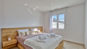 A bedroom with a wooden bed, white bedding, a nightstand with a lamp, and a window with a view.