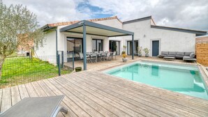Ett modernt hus med en swimmingpool, utomhusmöbler och en täckt uteplats.