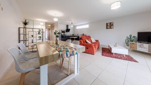 Una sala de estar moderna con comedor, un sofá rojo, televisor y cocina al fondo.