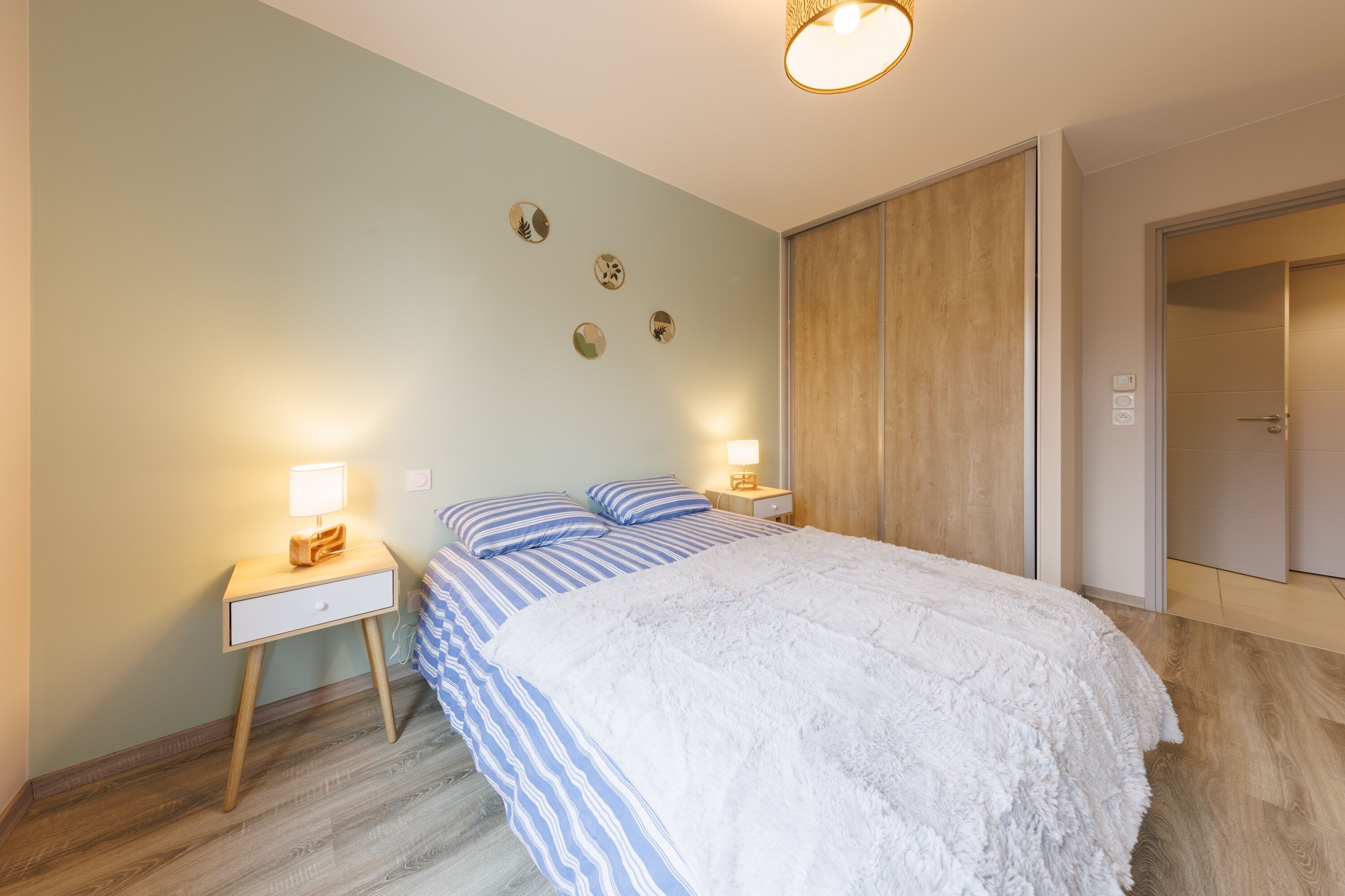 Quarto com cama, mesas de cabeceira, guarda-roupa e parede decorada com pratos.
