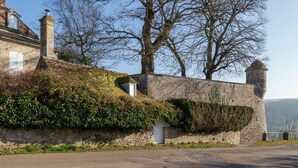Un mur de pierres recouvert de lierre, un ciel dégagé et une route devant.