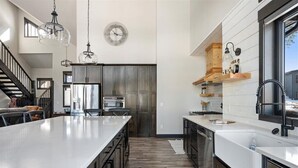 Een moderne keuken met een groot eiland, roestvrijstalen apparatuur en houten kastjes.