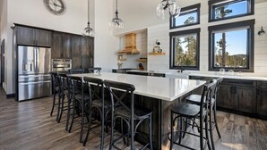 Een moderne keuken met een groot eiland, donkerhouten kasten, roestvrijstalen apparatuur en grote ramen.