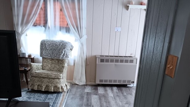 Una habitación con piso de madera, una silla, un escritorio y una ventana con cortinas traslúcidas.