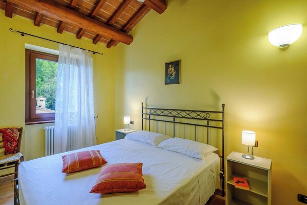 A bedroom with a bed, a nightstand, a window with curtains, and a wall-mounted light fixture.