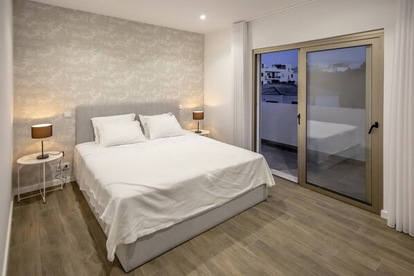 A modern bedroom with a large bed, two bedside lamps, and a sliding glass door to a balcony. - Krystal Bay Private Villa (Albufeira)