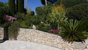 A stone pathway leading to a stone wall with a garden featuring various plants and flowers. - Beautiful house, very well located, sleeps 4 to 10, with swimming pool and air conditioning. (Saint-Raphaël)
