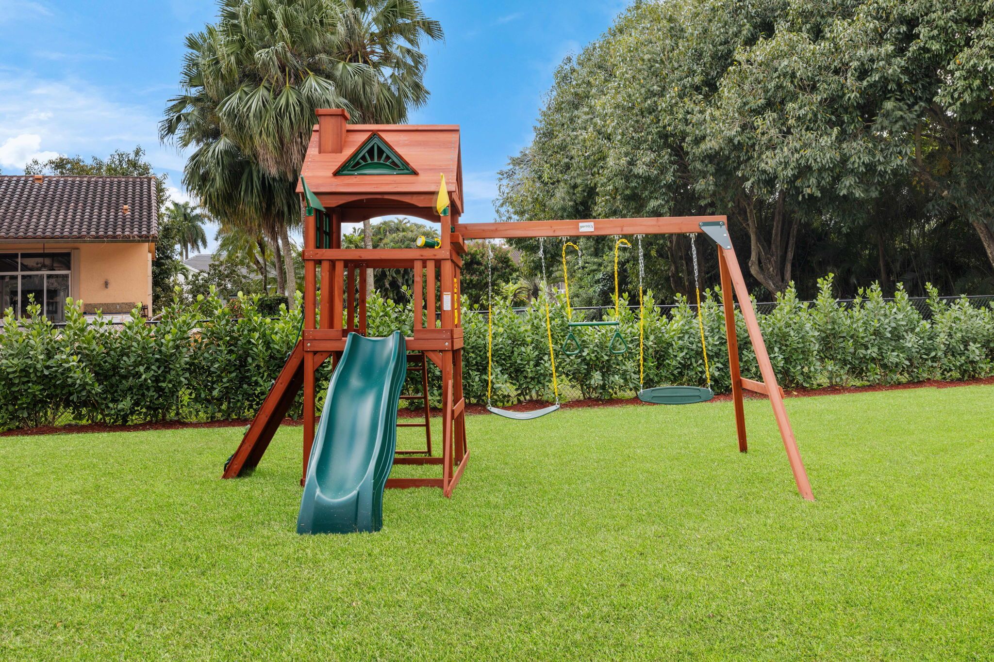 A playground with a slide and swings, surrounded by a well-maintained lawn and trees.