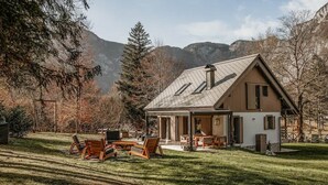 Ein Haus mit geneigtem Dach, einer Terrasse mit Gartenmöbeln und einer bergigen Kulisse.