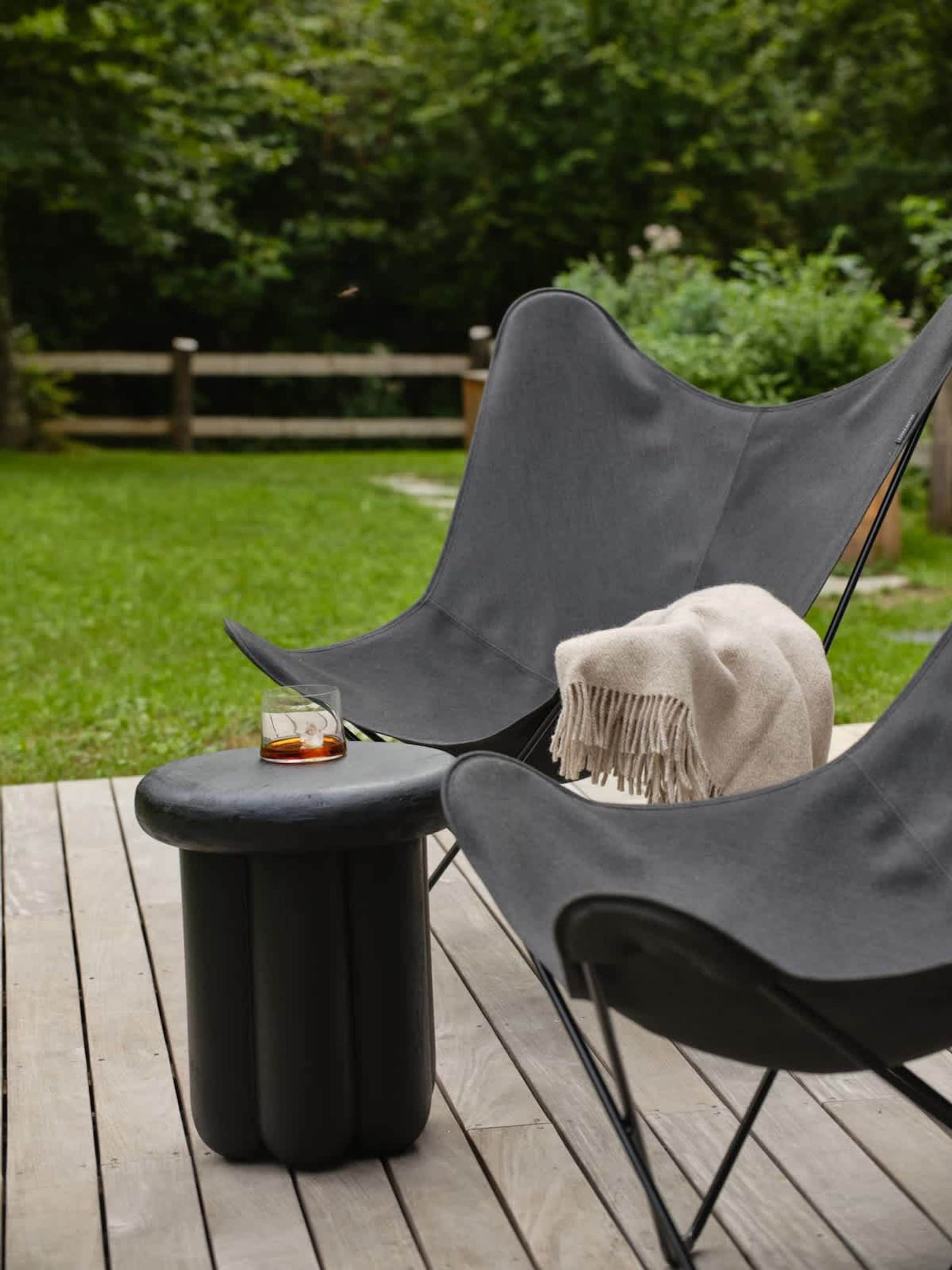 A deck with two black lounge chairs, one with a white throw blanket, and a small round table with a glass and a candle.