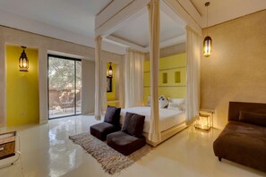 A bedroom with a four-poster bed, a sitting area with a small table, and a view through a sliding glass door.
