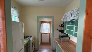 A narrow kitchen with a stove, refrigerator, and wooden cabinets.