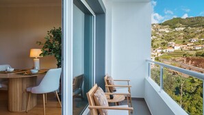 A balcony with a dining area, a chair, a small table, and a view of a hillside town. - GuestReady - A sweet escape in Caniço (Caniço)