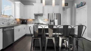 A modern kitchen with white cabinetry, stainless steel appliances, and a central island with bar stools. - Texas Cities Themed House, Hot tub. Don't Mess With Texas (Houston)