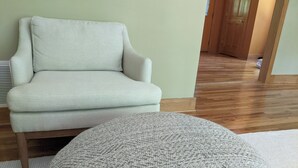 Una habitación con un sillón de color claro y un otoman tejido redondo.