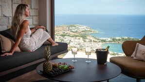 A woman sitting on a sofa with a view of the sea and a cityscape.