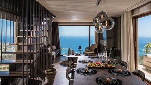 A modern dining area with a panoramic ocean view, featuring a wooden table set with plates, glasses, and a variety of dishes.