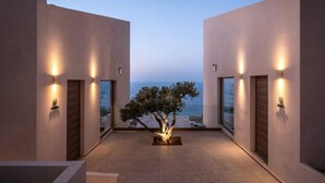 Ein modernes Gebäude mit einem zentralen Baum, beleuchteten Wänden und Blick auf das Meer.