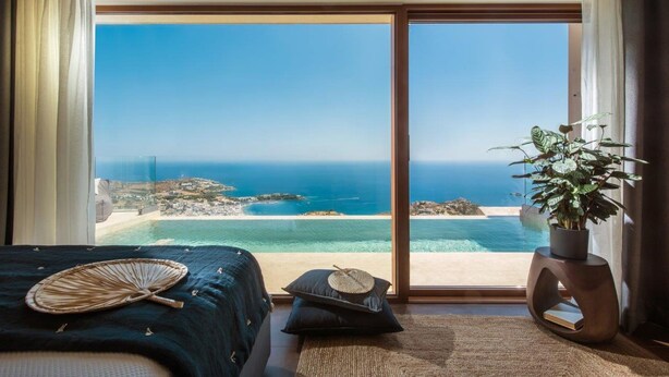 Ein Schlafzimmer mit einer großen Schiebeglastür, die auf einen Balkon mit Blick auf das Meer und den Strand führt.