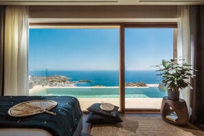 A bedroom with a large sliding glass door leading to a balcony with a view of the sea and a beach. - Villa Ouranos - Where the World Unfolds Before you (Malevizi)