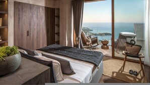 Ein modernes Schlafzimmer mit einem großen Bett, einer Sitzecke mit Meerblick und einem Balkon mit Stuhl und Tisch.