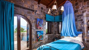 Un dormitorio con pared de piedra, cama con dosel azul, un cuadro y vistas a través de un ventanal.