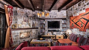 Una habitación acogedora con pared de piedra, vigas de madera en el techo, chimenea, televisor y estantería.
