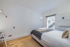 Un dormitorio con cama, una silla, un ventanal y un radiador.
