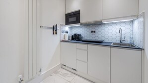 A modern kitchen with white cabinets, a black oven, and a hexagonal tile backsplash. - The Fairytale - Fitzrovia - by Frankie Says (London)