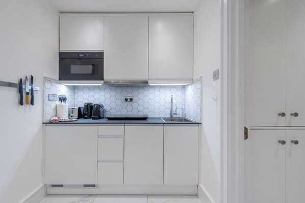 A compact kitchen with white cabinets, a microwave, a toaster, and a coffee maker.