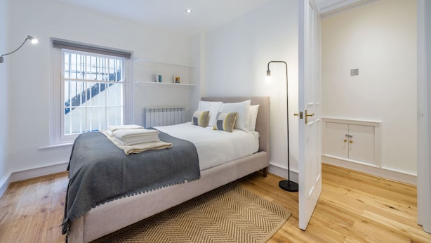 A bedroom with a bed, a window, a radiator, a floor lamp, and a wardrobe. - The Fairytale - Fitzrovia - by Frankie Says (London)