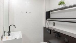 A modern bathroom with a white sink, black faucet, and a mirror. There is a shelf with a plant and a towel rack.